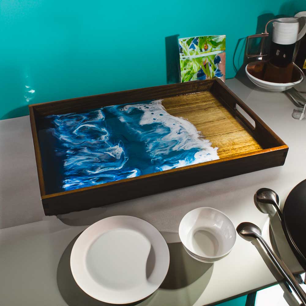 Wood serving tray with resin ocean painting on counter with plates and other dishes.