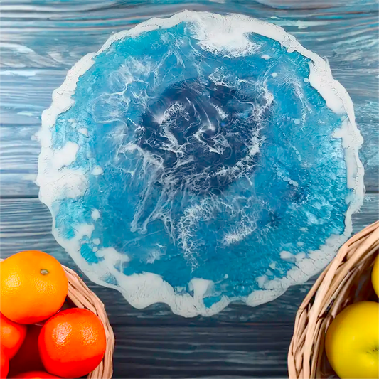 The ocean inspired trivet or centerpiece, resting on a table next to fruit baskets, has geode shaped edges, measures 13 inches round, and is made of epoxy resin. 